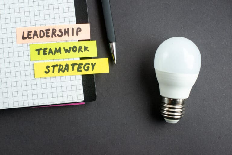 Billede af en lyspære med en blok og en kuglepen hvor der står leadership, teamwork, strategy, som afspejler det deltagerne lærer på et Copilot kursus til ledere
